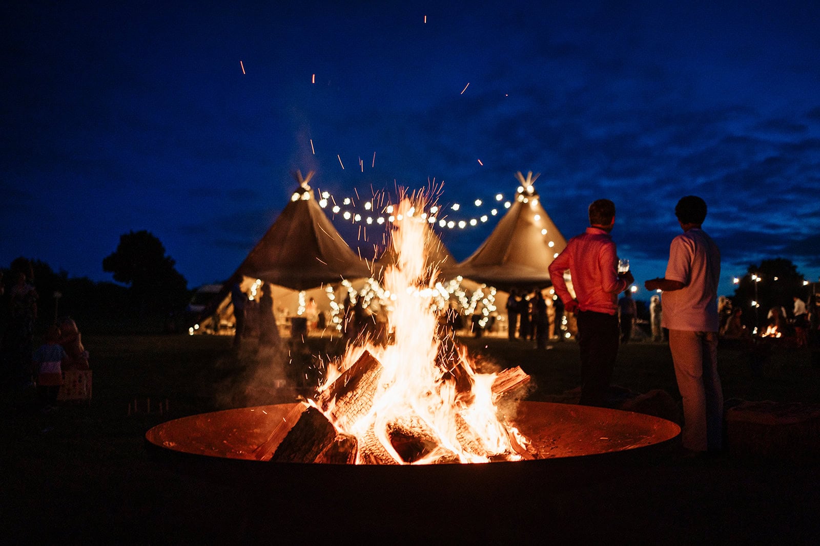 Bonfire gathering near tents under evening sky.