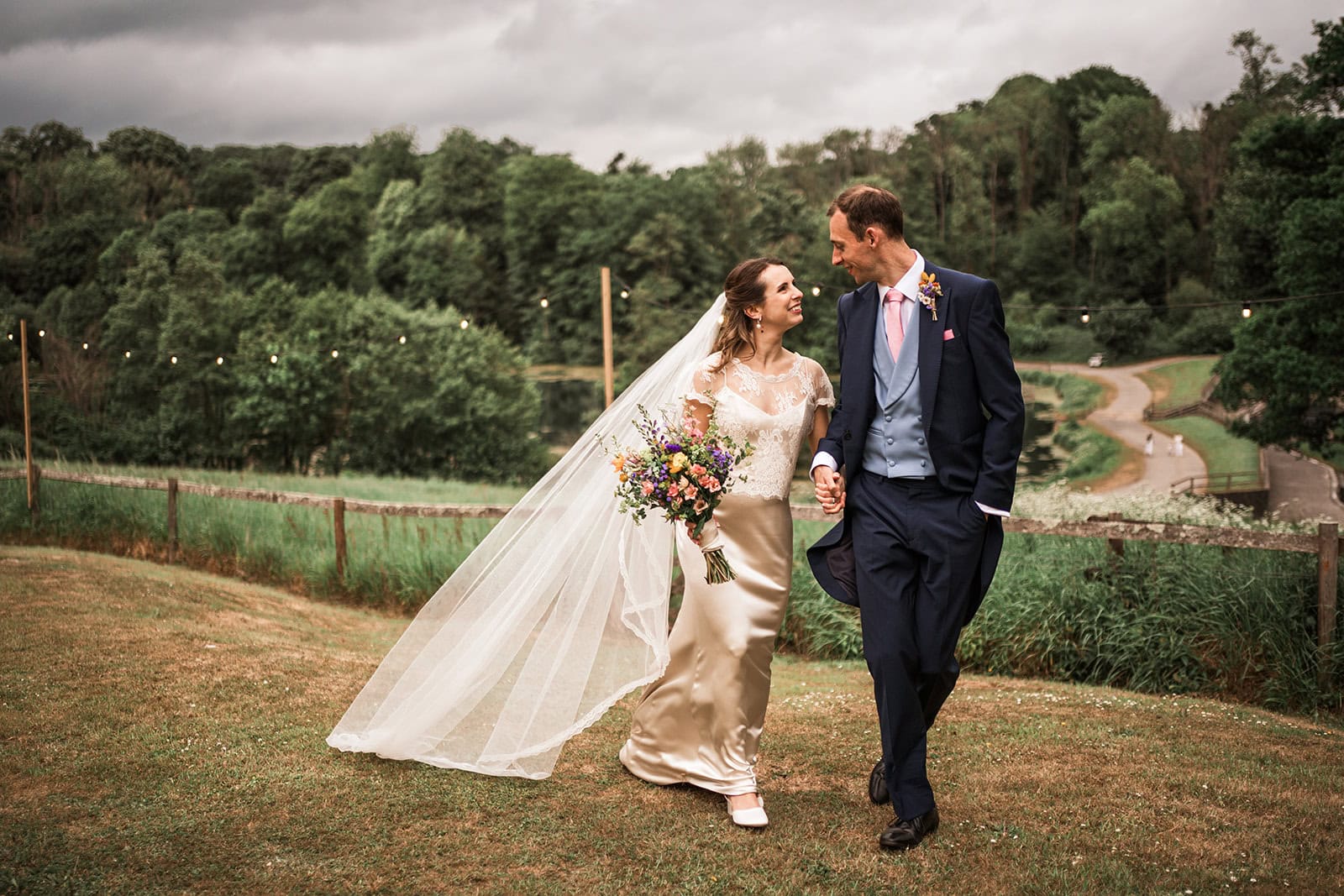 Elegant Ashley Wood Farm wedding couple walking outdoors with bridal bouquet, lush greenery background, romantic atmosphere.